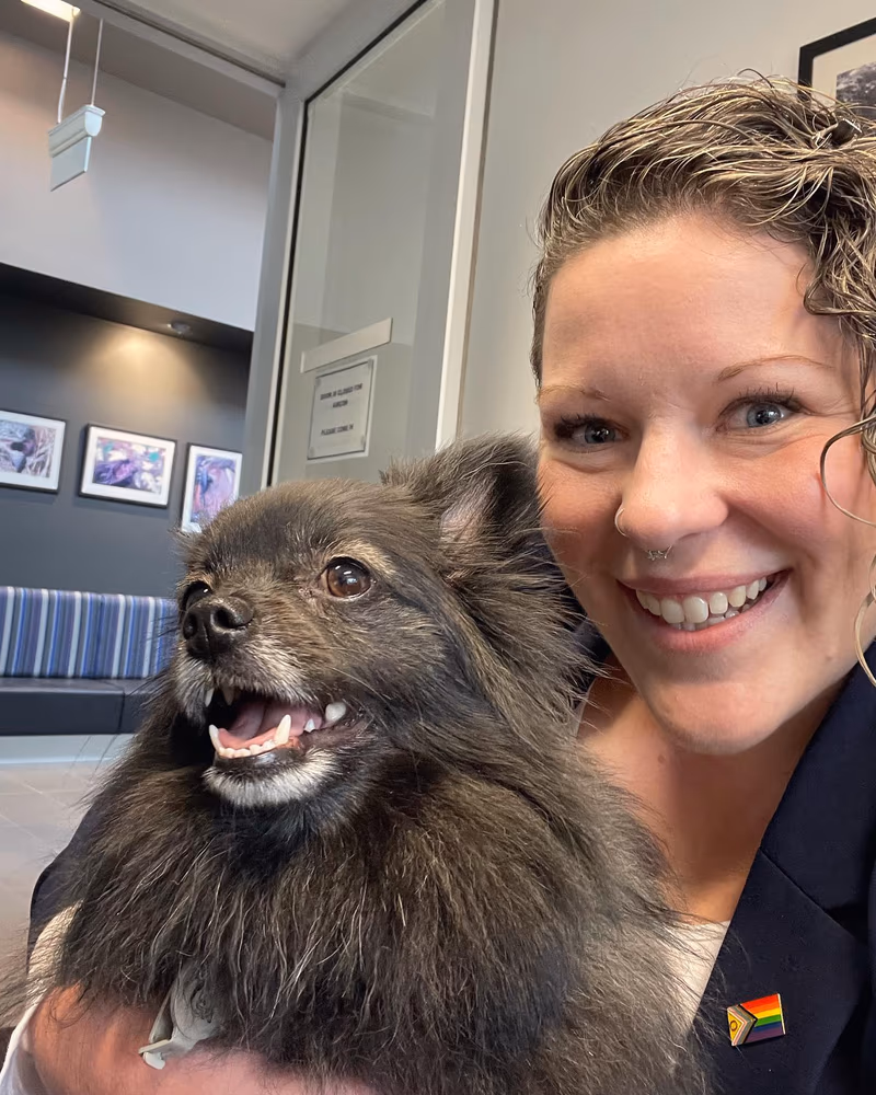 Dr Chantelle McGowan holding a relaxed pomeranian, wearing a progress pride flag pin